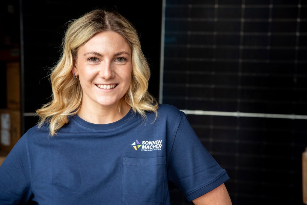 Frau in Solarenergie-T-Shirt lächelt vor Solarpanelen.